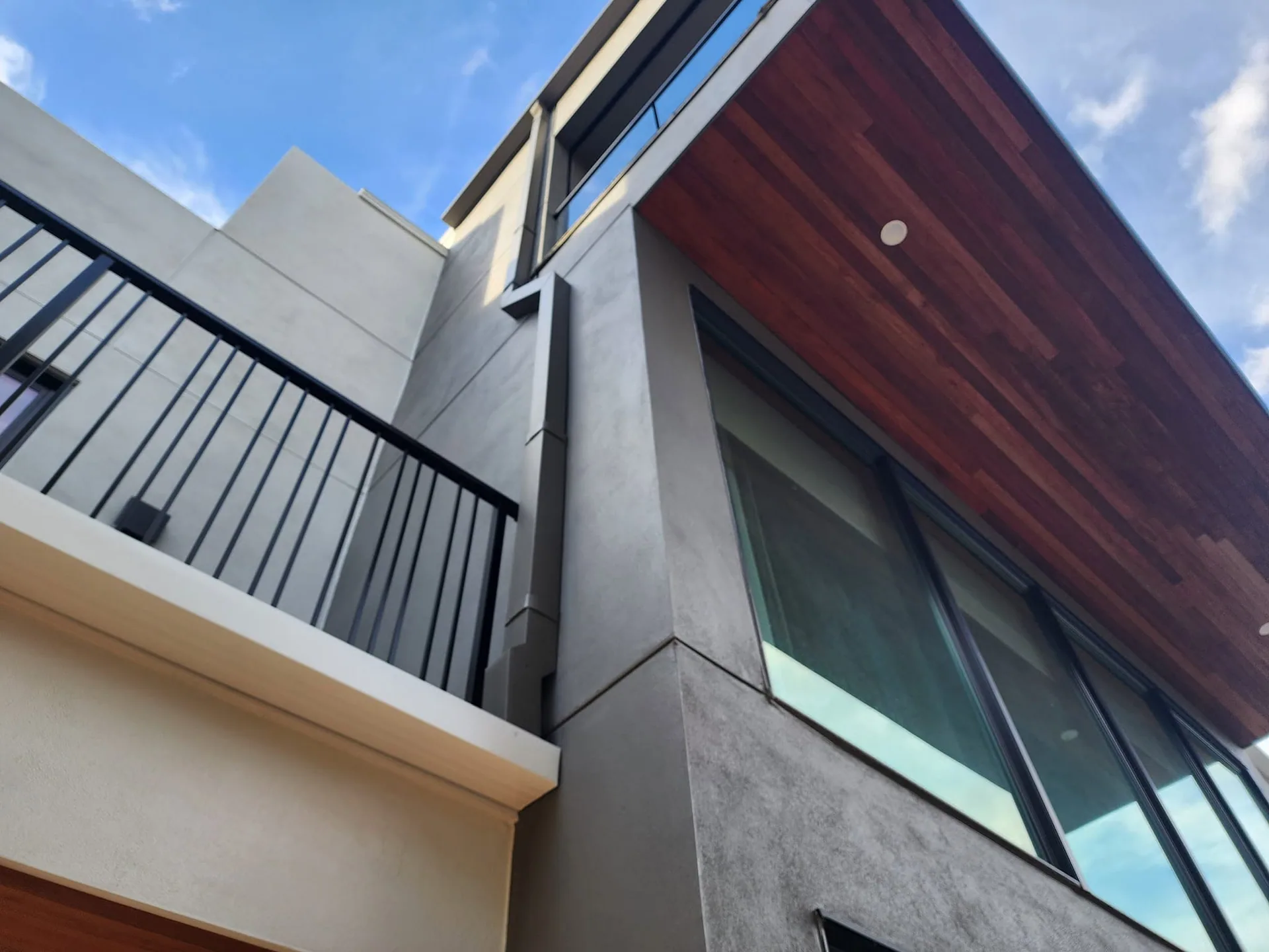 Low angle gray square downspout balcony railing wood soffit modern home, Sanford